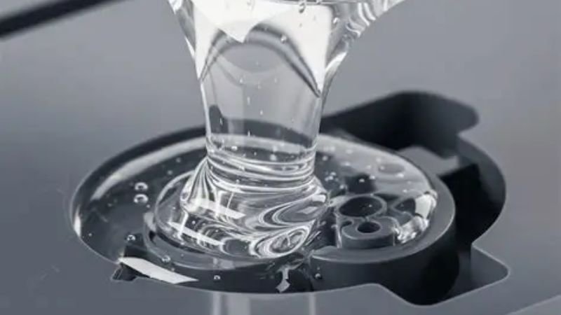 Close-up of transparent liquid silicone rubber being dispensed into a mold during the silicone molding process.