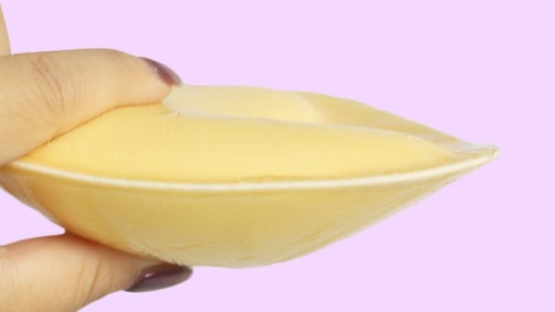 Silicone breast enhancer insert held from the side to show its thickness and tapered edge